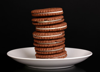 Chocolate cookies with creamy layer on plate isolated on black