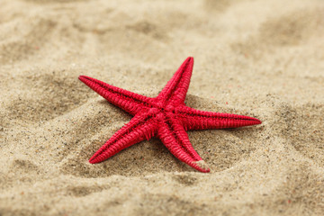 Close-up of a red starfish on beach sand pattern