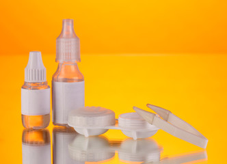 Eye drops and lenses on orange background