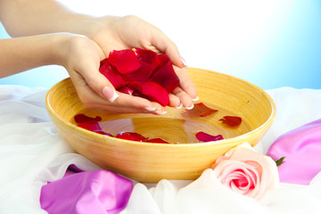 woman hands with wooden bowl of water with petals,