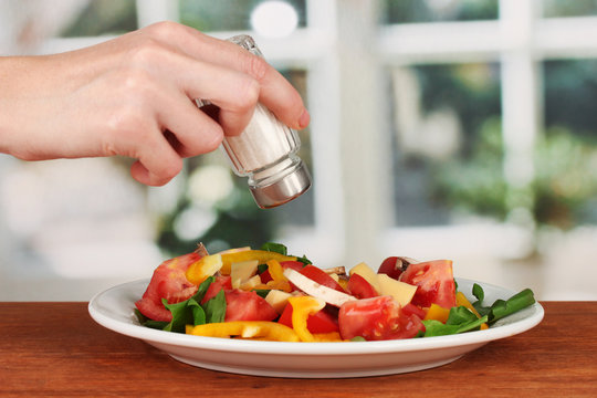 Hand adding salt using  salt shaker on bright background