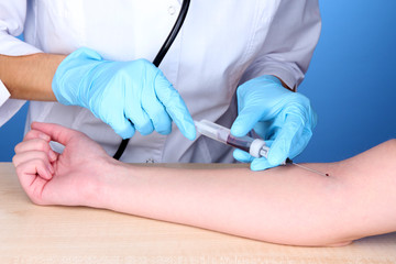 Nurse takes blood from the veins on blue background