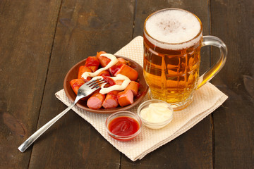 Beer and grilled sausages on wooden background
