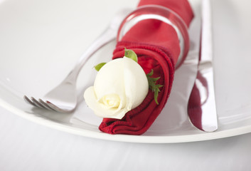 Closeup of  white rose and cutlery on white plate 