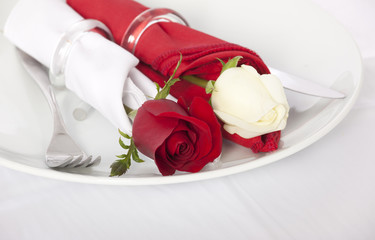 Closeup of red and white rose and cutlery on white plate