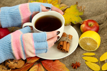 hands holding cup of hot drink and autumn leaves,