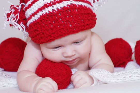 The baby in a red knitted cap against yarn balls (3 months)