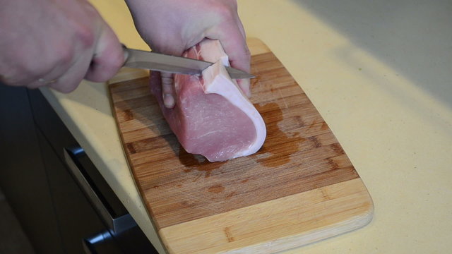 Man hands cut pork saddle meat on table board into pieces