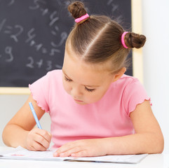 Little girl is writing using a pen