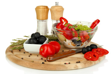 Fresh greek salad in glass bowl surrounded by ingredients for