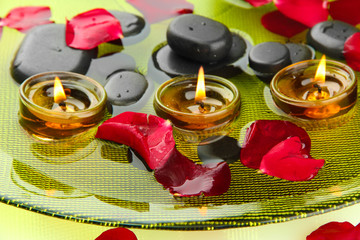 spa stones with rose petals and candles in water on plate