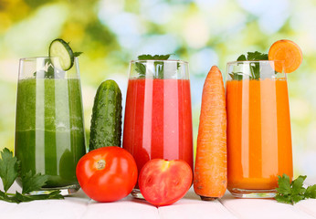Fresh vegetable juices on wooden table, on green background