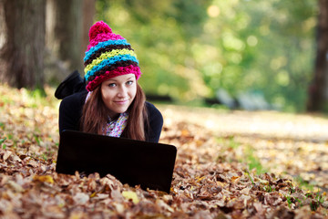 Beautiful teenage girl working on laptop in park during autumn