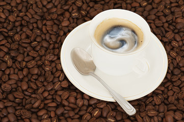 cup of coffee with teaspoon on coffee beans background