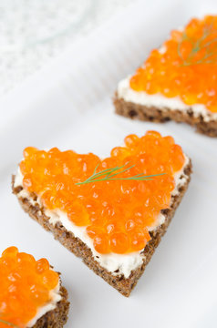 sandwich with red caviar in the form of a heart on white plate