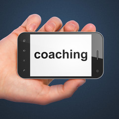 Hand holding smartphone with word coaching on display. Generic m