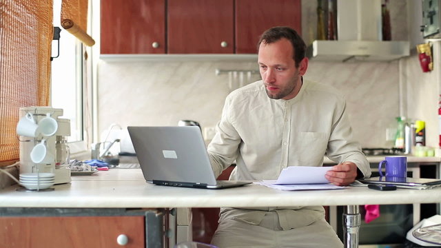 Young sad man counting bills on laptop computer in home