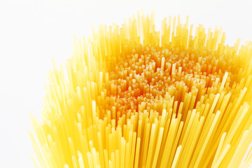Close up of dry yellow uncooked spaghetti on white background.