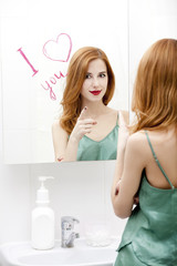 Redhead girl near mirror with heart it in bathroom.