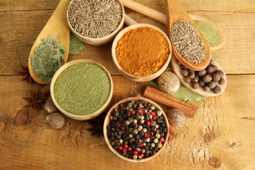 bowls and spoons with spices, on wooden background