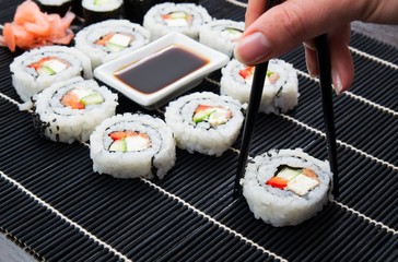 Woman's hand taking philadelphia sushi. Black mat in background