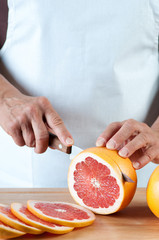 Vertical shot of female hands slicing a fresh grapefruit