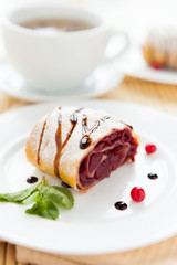 cherry strudel on white plate and a cup of tea
