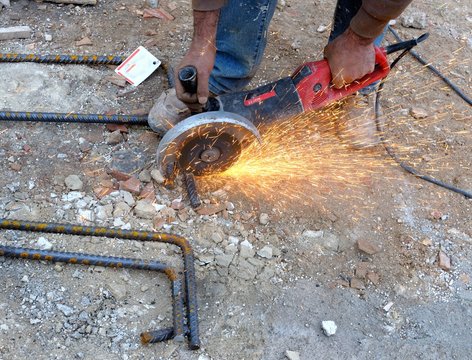 Construction worker cuts rebar circular saw on site.