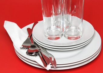 Pile of white plates, glasses, forks, spoons.
