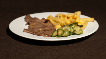 a plate with a steak, potatoes and zucchini