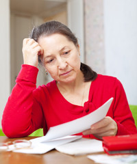 serious mature woman reads payments  at home