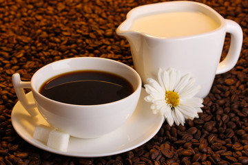 A cup of strong coffee and sweet cream on coffee beans close-up