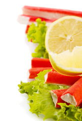 Crab sticks on lettuce leaves with lemon, isolated on white
