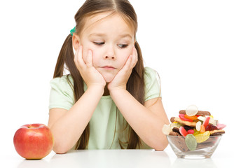 Little girl choosing between apples and sweets
