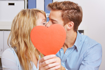 Paar küsst sich hinter einem roten Herz