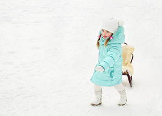 Little girl pulling her sledge in winter day