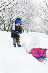 Fototapeta na wymiar Little boy sledding in snow forest
