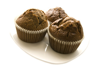 Three gingerbread muffins in cups on a plate.