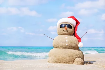 Smiling sandy snowman in red santa hat on the sea beach. © EMrpize
