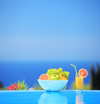 Glass of juice and bowl of various fruits next to a swimming poo