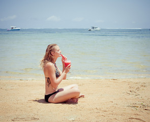 relaxing woman sitting on sand with cocktail 