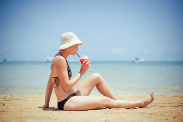relaxing woman sitting on sand with cocktail 