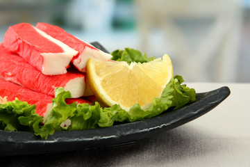 Crab sticks with lettuce leaves and lemon on plate, close up