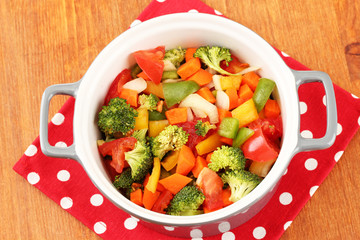 Vegetable stew in gray pot on color napkin on wooden background