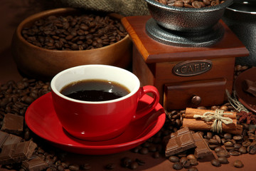 cup of coffee, grinder and coffee beans on brown background