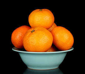 Tasty mandarines in color bowl isolated on black