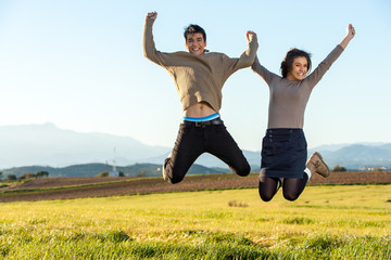 Teen couple jumping outdoors.