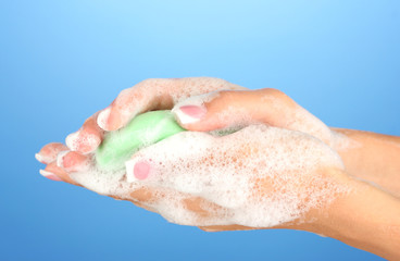 Woman's hands in soapsuds, on blue background close-up