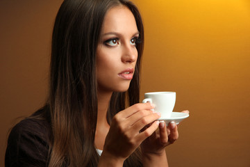 beautiful young woman with cup of coffee, on yellow background