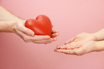 Fototapeta na wymiar Czerwone serce w ręce kobiety i mężczyzny, na różowym tle